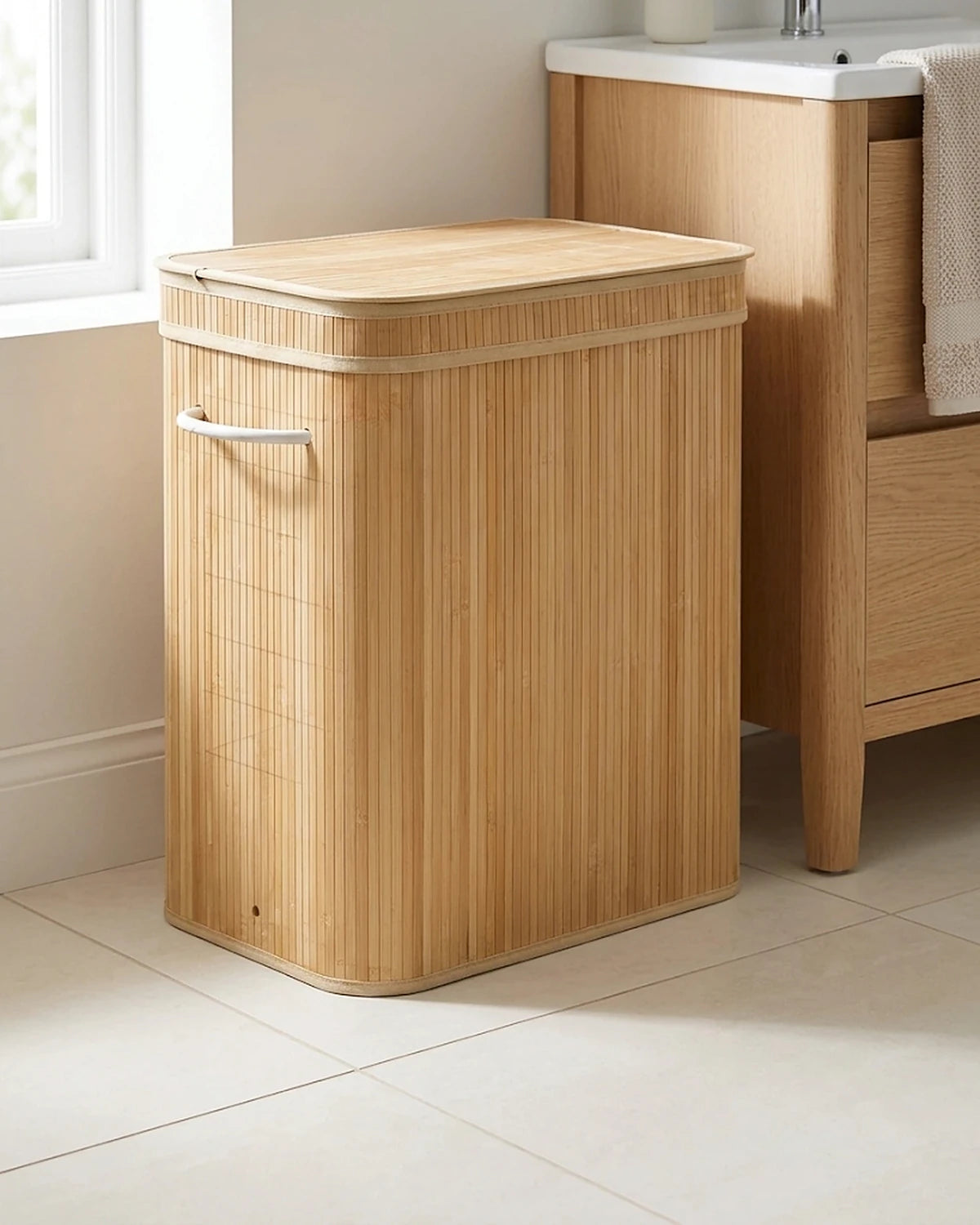 Panier à linge bambou 90 L, couvercle fermé, posé dans une salle de bain près d'un meuble vasque en bois