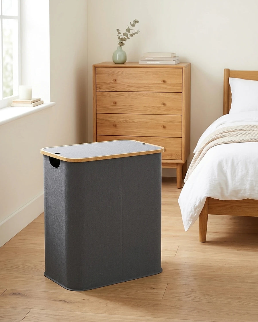 Panier à linge pliable 80 L gris dans une chambre, près d'une commode en chêne et d'un lit