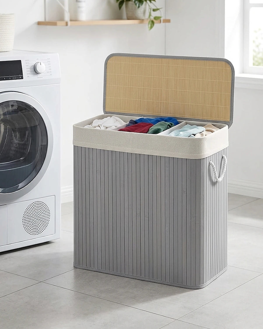 Panier à linge 150 L gris à 3 compartiments, couvercle en bambou ouvert, à côté d'un sèche-linge