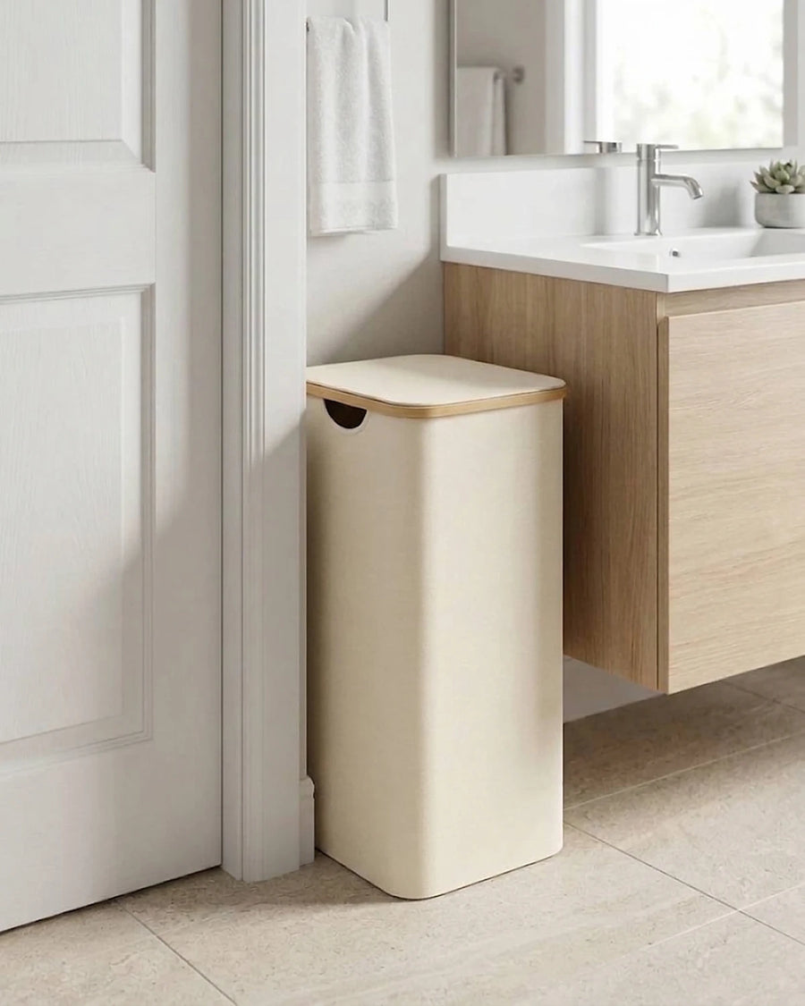 Panier à linge étroit 65 L beige avec couvercle, glissé entre une porte et un meuble de salle de bain